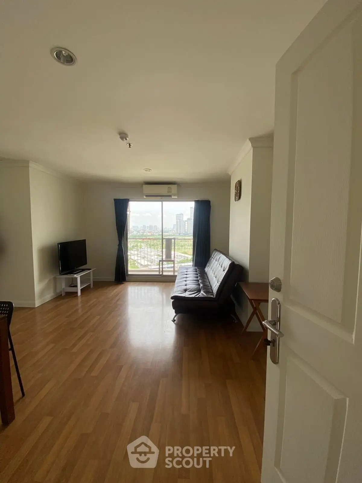 Spacious living room with balcony and city view, featuring wooden flooring and modern furnishings.