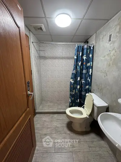 Cozy bathroom with shower and toilet, featuring a playful shower curtain and wooden door.