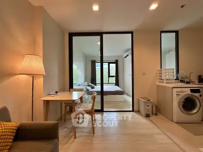 Modern open-plan living room with cozy dining area and view into a stylish bedroom, featuring a washing machine.