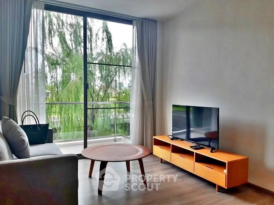 Modern living room with large window and stylish furniture overlooking greenery.