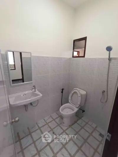 Modern bathroom with white tiles, wall-mounted sink, and shower head in a minimalist design.