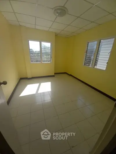 Bright empty room with yellow walls and tiled floor, featuring two windows for natural light.