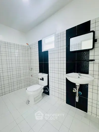 Modern bathroom with sleek black and white tiles, featuring a toilet and wall-mounted sink.