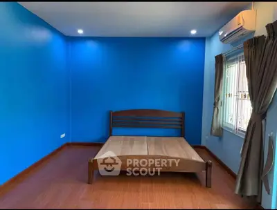 Spacious bedroom with vibrant blue walls and wooden flooring, featuring a wooden bed frame and air conditioning.