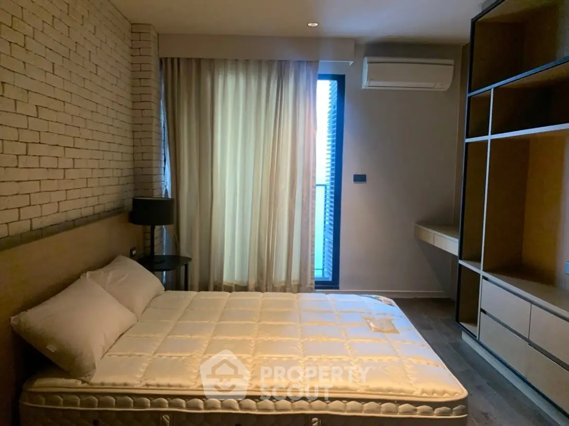 Modern bedroom with brick accent wall and built-in storage, featuring a cozy bed and natural light.