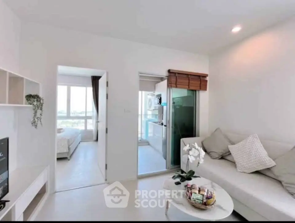 Modern living room with cozy sofa, open layout to kitchen and bedroom, bright natural light.