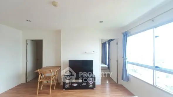 Bright living room with wooden flooring and large window, featuring a TV and dining area.