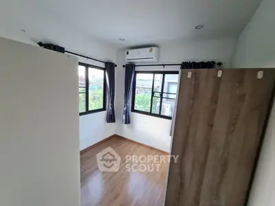 Bright bedroom with wooden flooring and large windows, featuring an air conditioning unit for comfort.