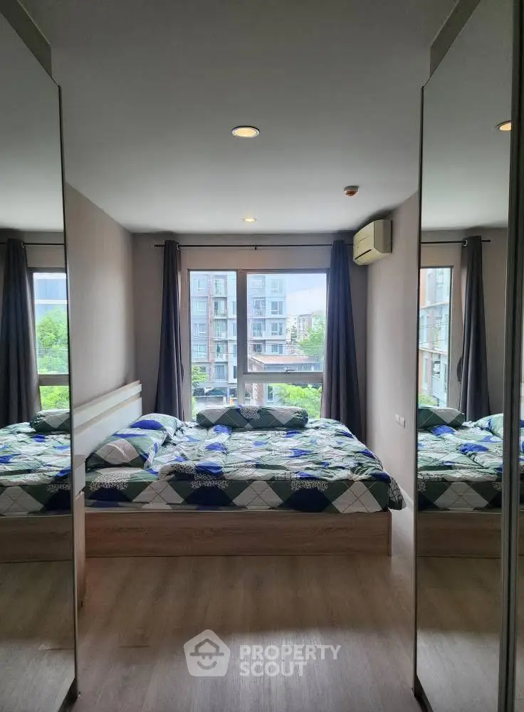 Modern bedroom with large windows and mirrored closets in urban apartment.