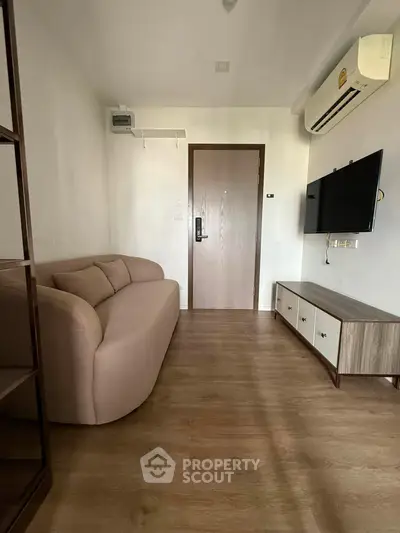 Modern living room with sleek furniture and wall-mounted TV, featuring wooden flooring and air conditioning.
