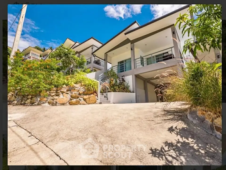 Stunning modern hillside home with spacious driveway and lush landscaping under a clear blue sky.