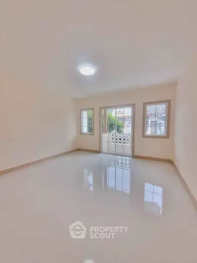 Spacious empty room with glossy tiled floor and large windows offering natural light.