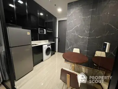 Modern kitchen with sleek black cabinets, stainless steel fridge, and washing machine