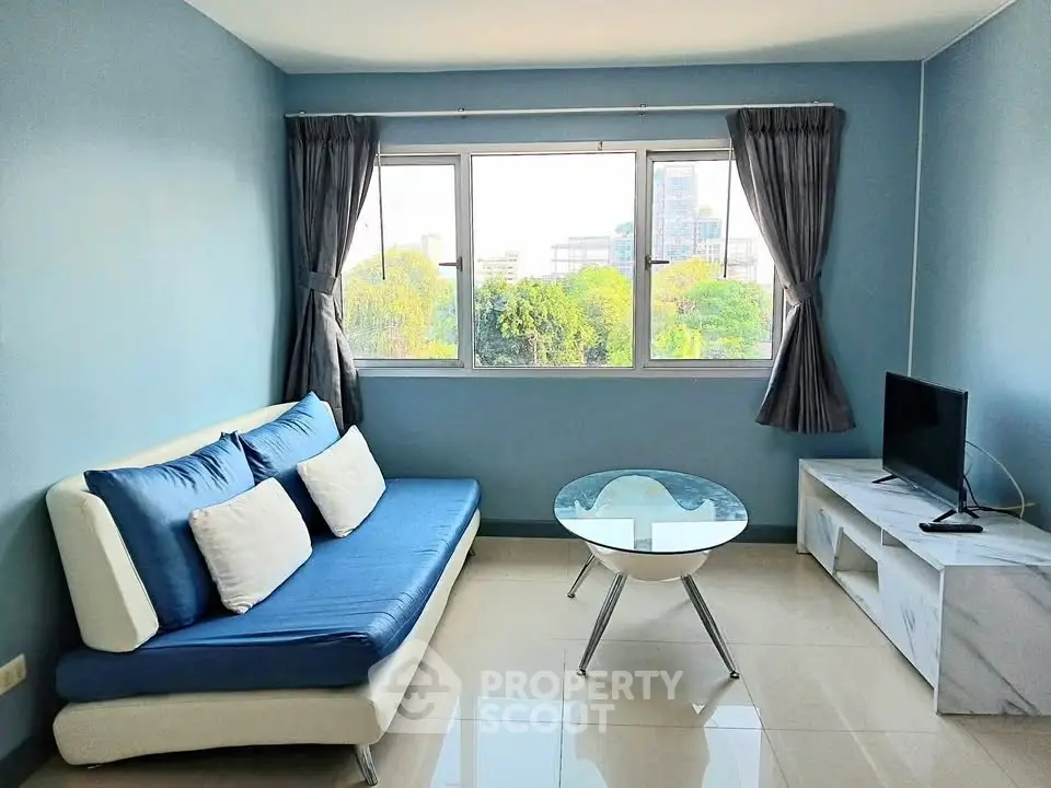 Bright living room with modern blue sofa, glass coffee table, and large window with city view.