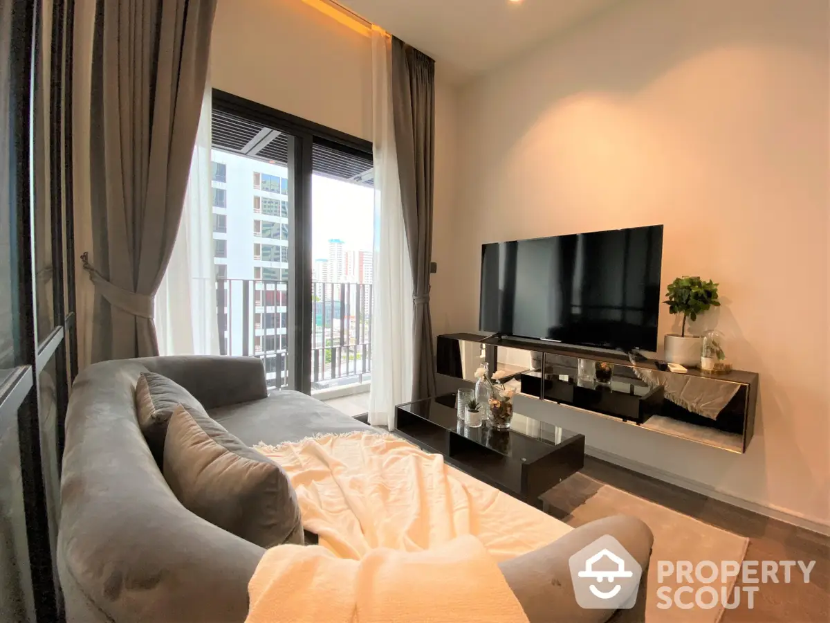 Modern living room with plush sofa and large flat-screen TV, leading to a sunny balcony with urban views, perfect for relaxation and entertainment.