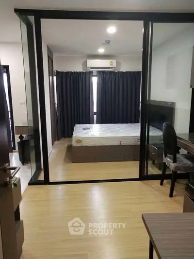 Modern bedroom with glass partition and wooden flooring in stylish apartment.