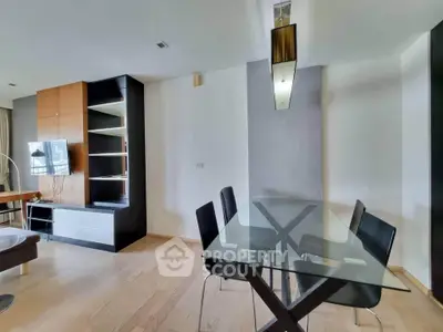 Modern dining area with glass table and sleek black chairs in open-plan living space.