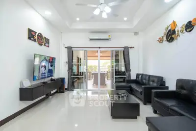 Spacious modern living room with sleek black leather furniture and large TV, leading to a bright balcony.