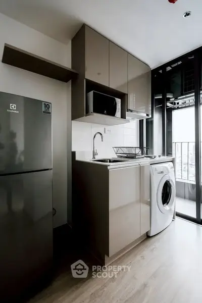 Modern kitchen with sleek cabinets, washing machine, and balcony view in a stylish apartment.