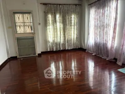 Spacious empty room with polished hardwood floors and large windows with curtains.