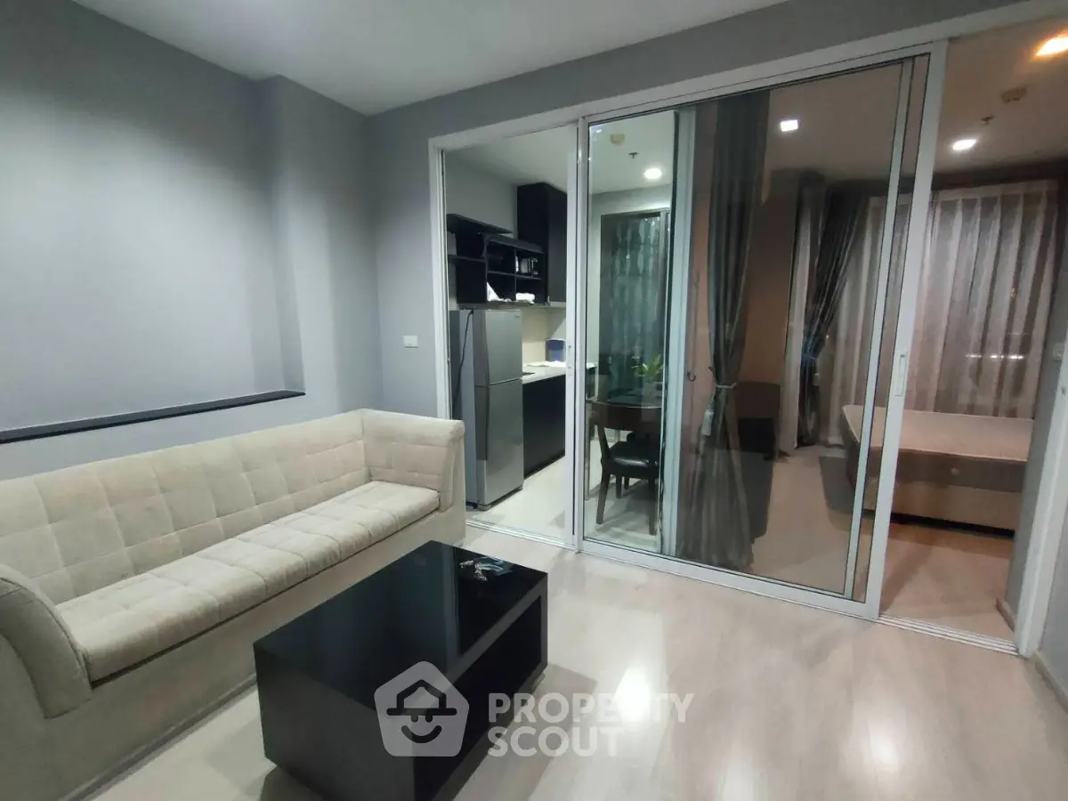 Modern living room with open layout to kitchen and bedroom, featuring sleek furniture and neutral tones.