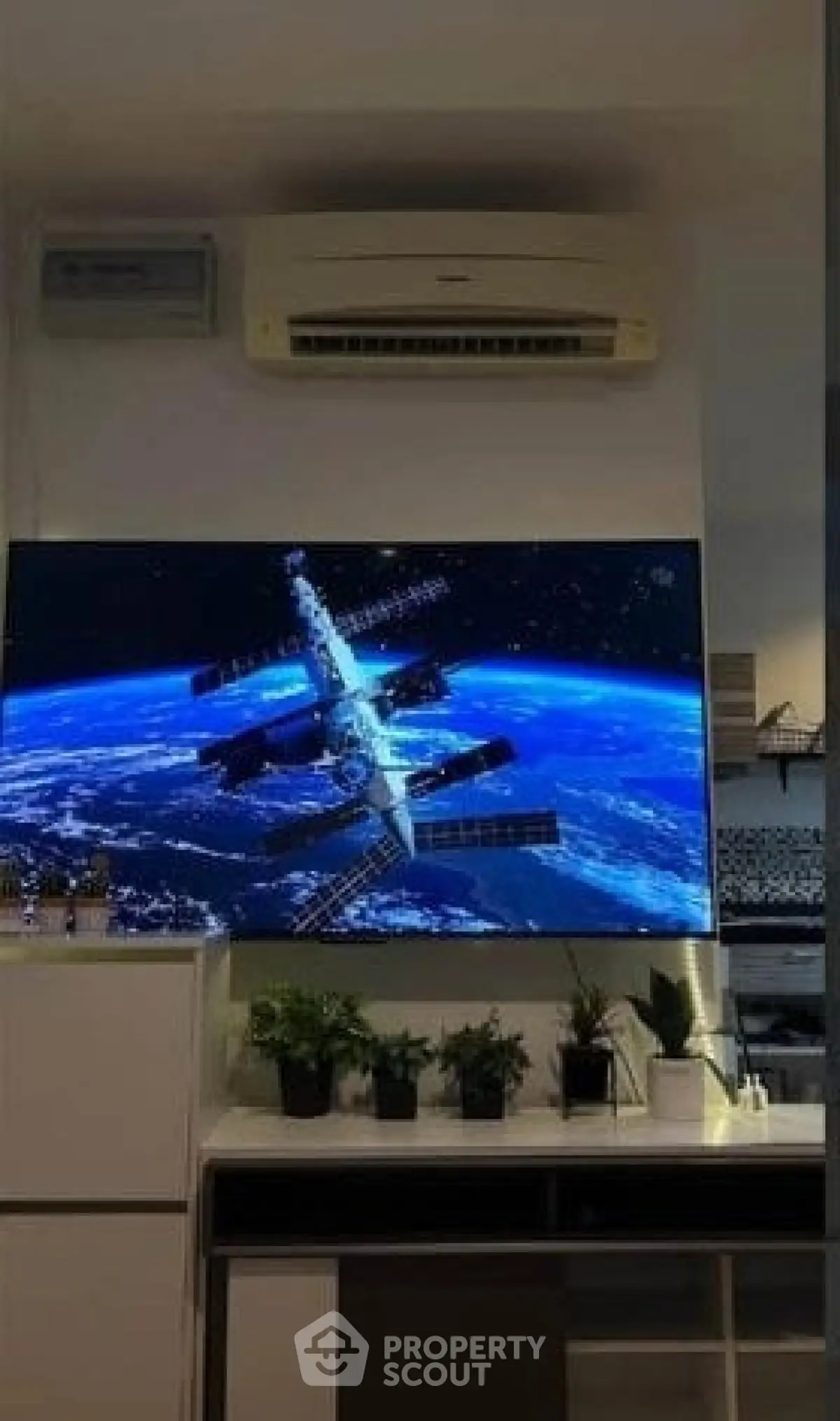 Modern living room with wall-mounted TV and air conditioning unit, featuring sleek cabinetry and decorative plants.