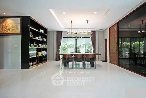 Spacious dining area with elegant chandelier and large windows overlooking greenery.