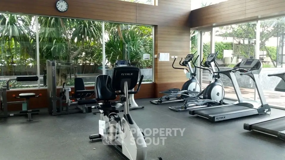 Spacious gym with modern exercise equipment and large windows offering garden views.