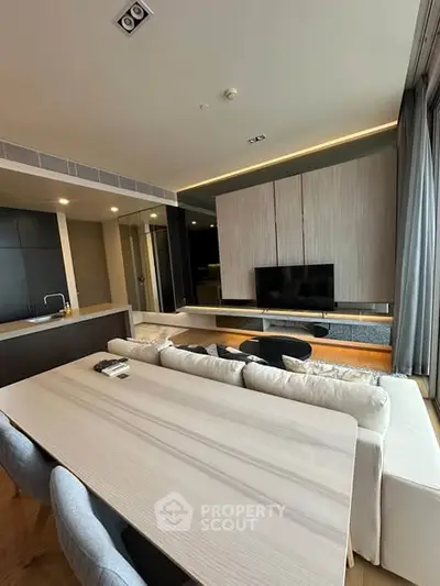 Modern open-plan living room with sleek kitchen and stylish dining area, featuring contemporary furniture and large windows.