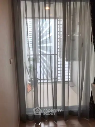 Modern apartment balcony with sheer curtains and city view.