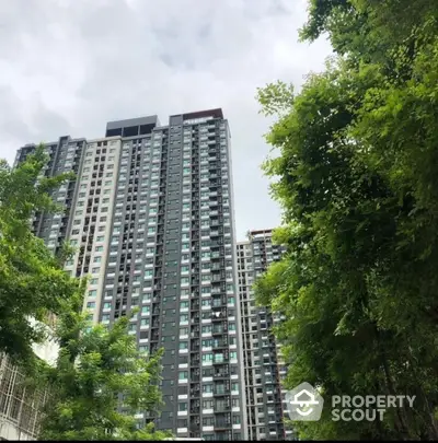 Modern high-rise apartment building with lush greenery and cloudy sky