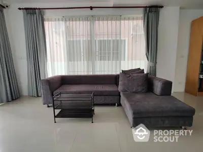 Spacious living room with large windows draped in sheer curtains, complemented by a plush L-shaped sofa and a modern coffee table.