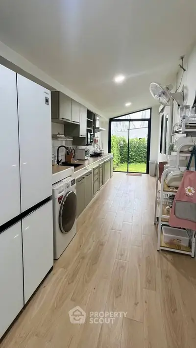 Modern kitchen with sleek appliances and garden view, featuring open layout and wooden flooring.