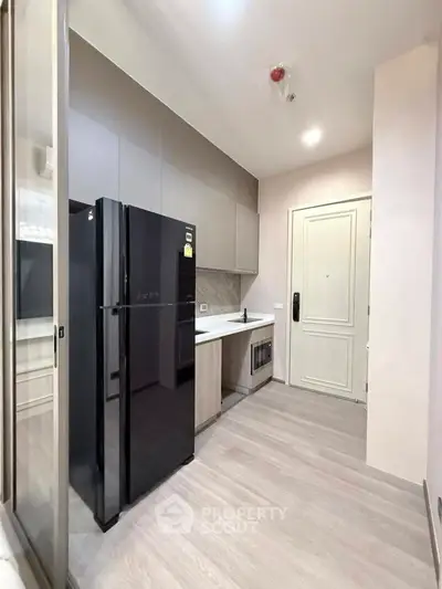 Modern kitchen with sleek black fridge and minimalist cabinetry in a stylish apartment.