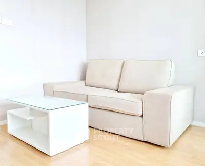 Modern living room with beige sofa and sleek glass coffee table on wooden floor.