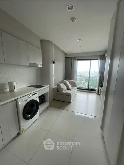 Modern apartment with sleek kitchen and cozy living area, featuring a washing machine and large window view.