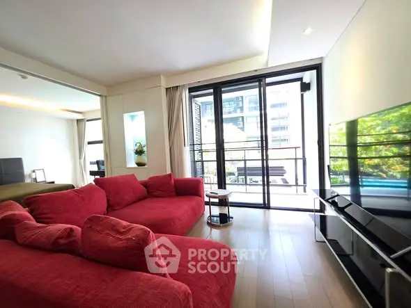 Spacious living room with red sofas and large windows offering a bright view.