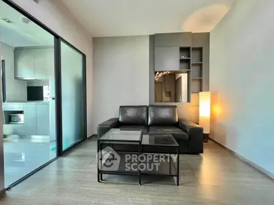 Modern living room with sleek black sofa and glass coffee table, adjacent to a stylish kitchen.