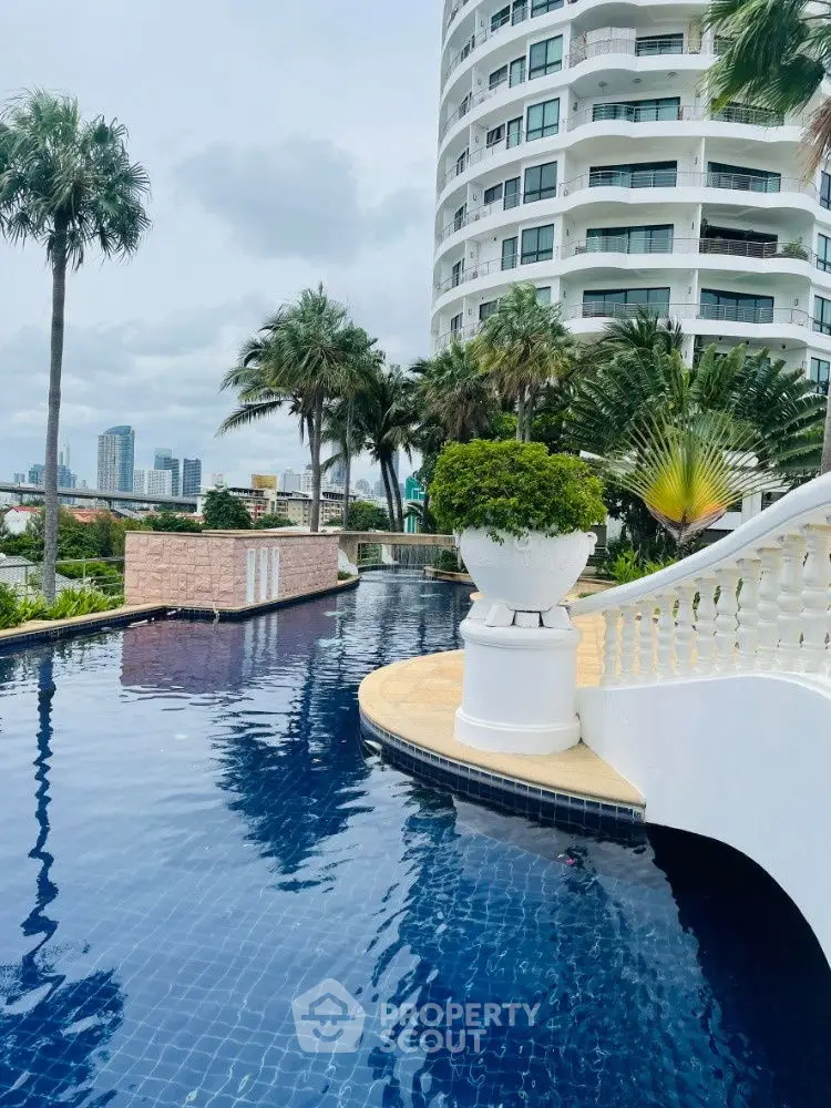 Luxurious poolside view with modern high-rise building and lush palm trees.