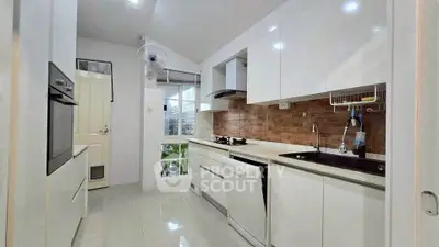 Modern kitchen with sleek white cabinets and brick backsplash, featuring built-in appliances and ample natural light.