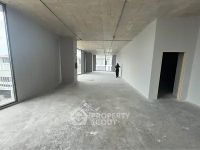 Spacious unfinished open-plan interior with large windows and concrete flooring, ideal for customization.