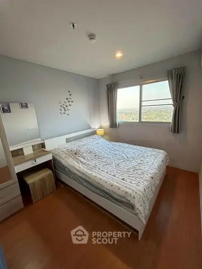 Cozy bedroom with wooden flooring and a large window offering a scenic view, perfect for relaxation.