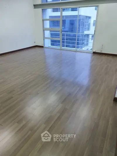 Spacious empty room with large windows and wooden flooring in modern apartment.