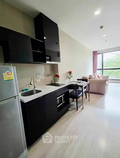 Modern open-layout kitchen with sleek black cabinets and cozy living area with large window view.