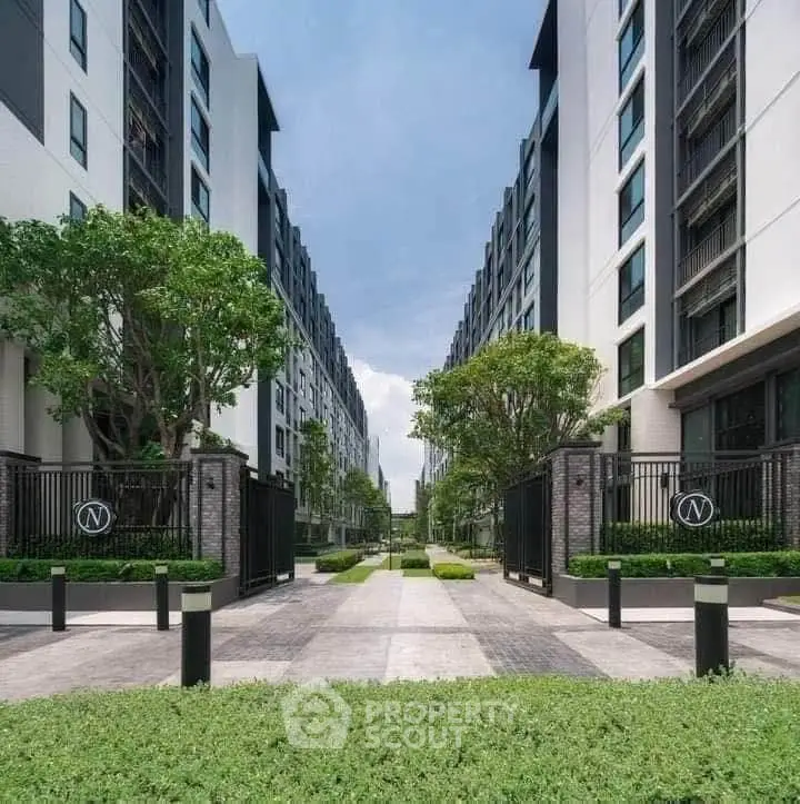 Modern apartment complex entrance with lush greenery and sleek architecture.