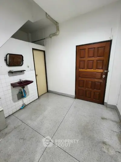Spacious utility room with sink and wooden door, ideal for storage or laundry setup.