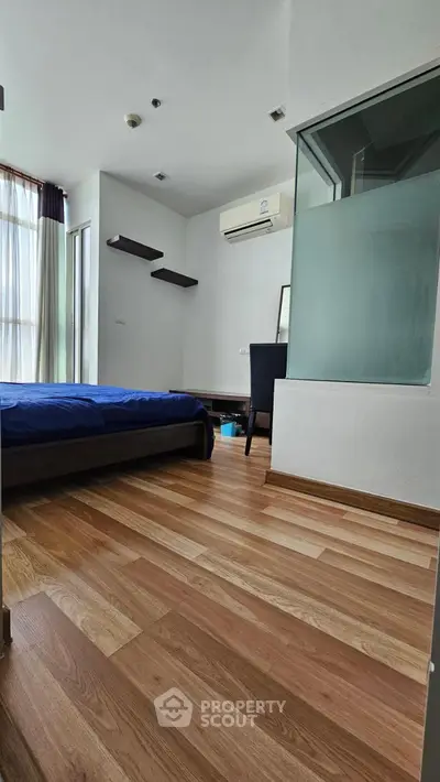 Modern bedroom with wooden flooring and large window, featuring a sleek air conditioning unit.