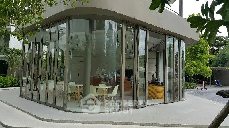 Modern glass-walled building with stylish interior seating and lush greenery.