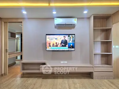 Modern living room with built-in wooden shelves and wall-mounted TV under air conditioning unit.
