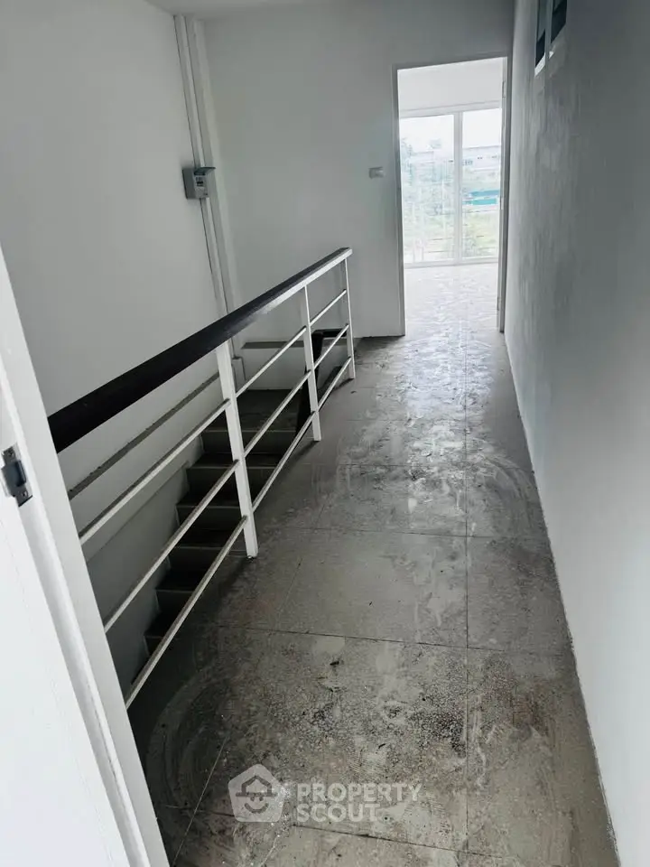 Spacious corridor with natural light and modern railing leading to a bright room with large windows.